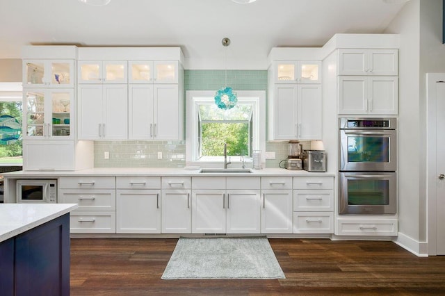 kitchen with sink, tasteful backsplash, double oven, pendant lighting, and white cabinets