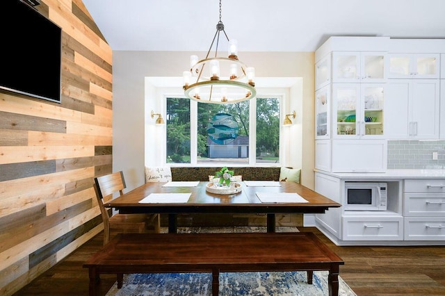 dining area featuring lofted ceiling, dark wood-type flooring, an inviting chandelier, breakfast area, and wood walls