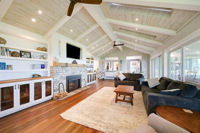 living room featuring built in shelves, a stone fireplace, vaulted ceiling with beams, ceiling fan, and hardwood / wood-style floors