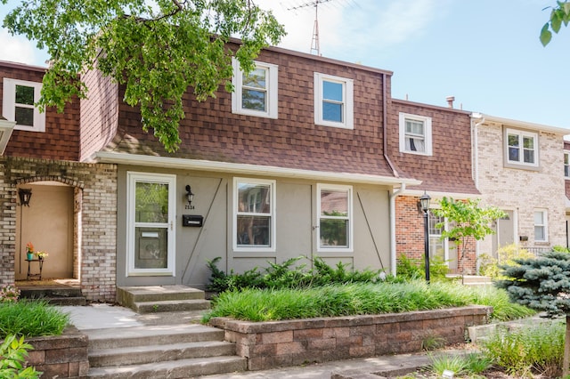 multi unit property with mansard roof, brick siding, roof with shingles, and stucco siding