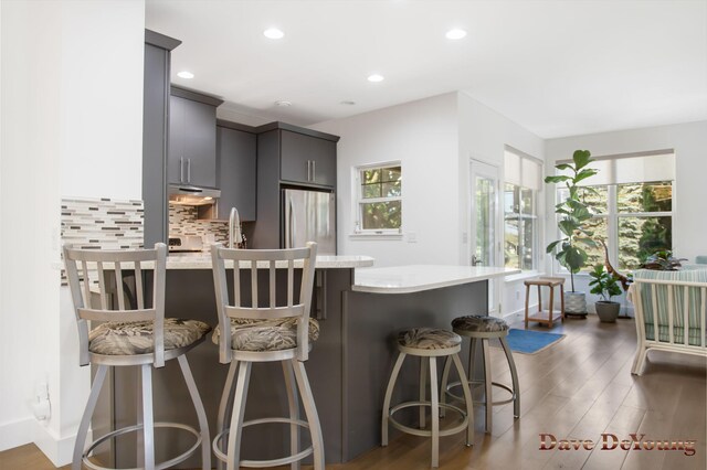 kitchen featuring light hardwood / wood-style flooring, sink, stainless steel refrigerator, decorative backsplash, and a kitchen breakfast bar