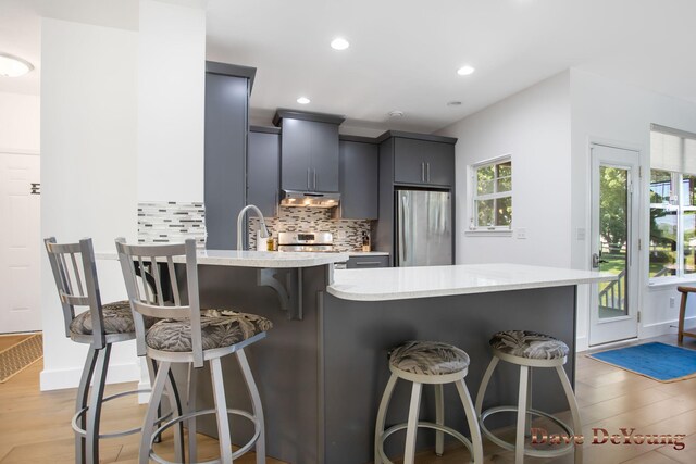 kitchen featuring stainless steel refrigerator, a kitchen breakfast bar, decorative backsplash, and light wood-type flooring