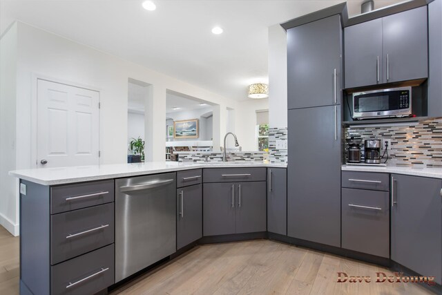 kitchen featuring appliances with stainless steel finishes, tasteful backsplash, sink, light wood-type flooring, and light stone countertops