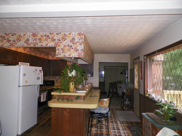 kitchen featuring white fridge, a breakfast bar area, dark brown cabinetry, and kitchen peninsula