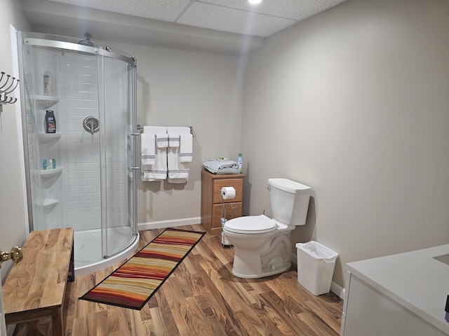 bathroom with hardwood / wood-style floors, a shower with door, a paneled ceiling, and toilet