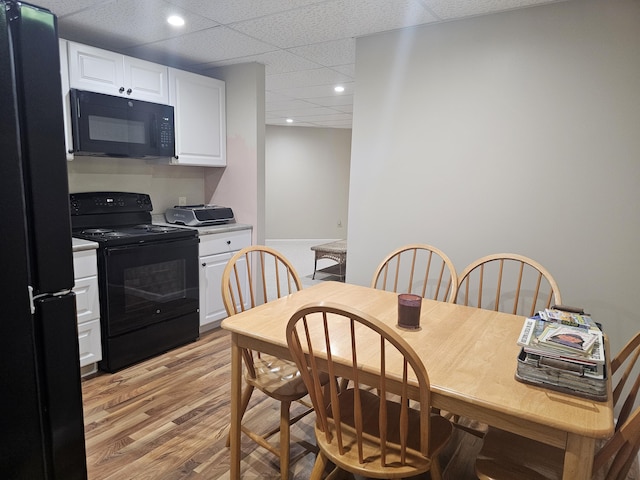 kitchen featuring a drop ceiling, white cabinetry, black appliances, and light hardwood / wood-style floors