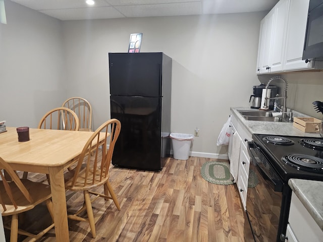 kitchen featuring sink, black appliances, light hardwood / wood-style floors, white cabinets, and a drop ceiling