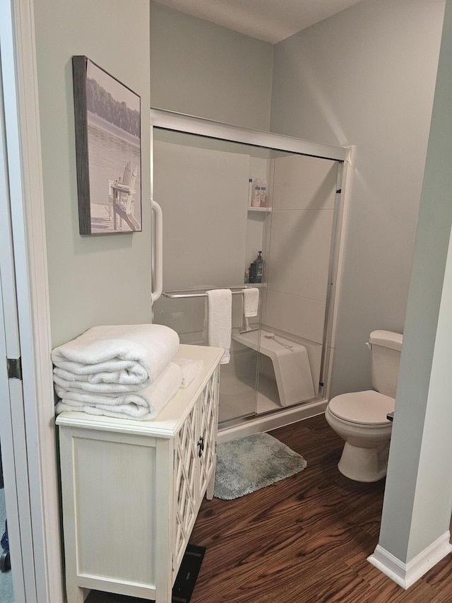 bathroom featuring hardwood / wood-style flooring, a shower with shower door, and toilet