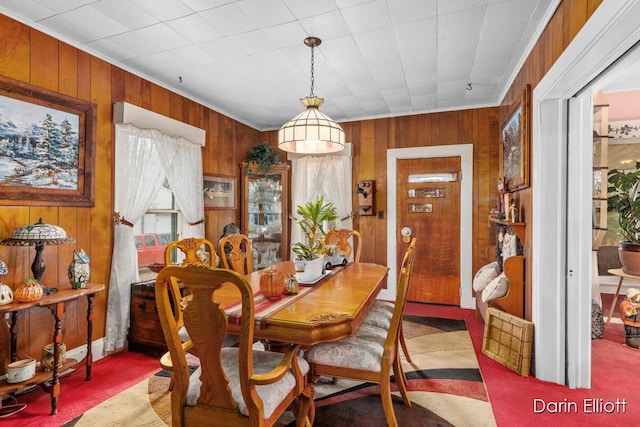 carpeted dining area featuring wooden walls