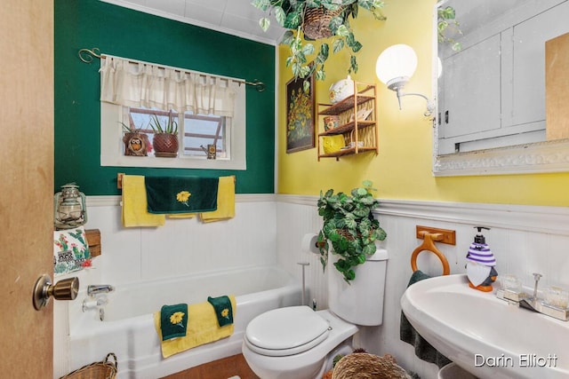 full bath featuring a tub to relax in, a wainscoted wall, toilet, and a sink