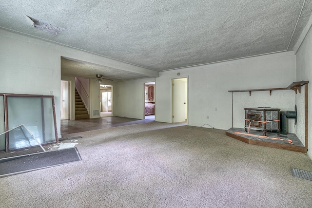 unfurnished living room featuring carpet flooring, a textured ceiling, and a wood stove