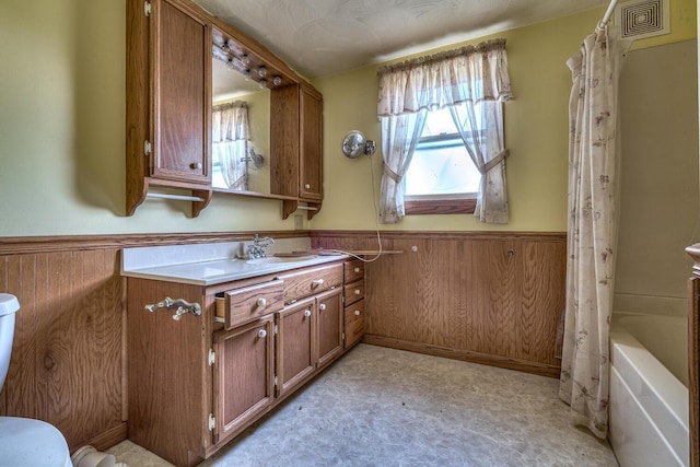 bathroom with vanity, shower / bathtub combination with curtain, and wood walls