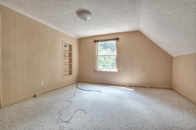 bonus room featuring lofted ceiling, built in features, a textured ceiling, and carpet flooring