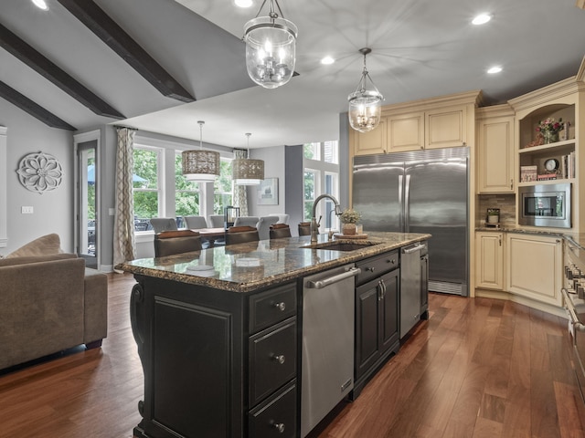 kitchen with built in appliances, open floor plan, dark cabinets, cream cabinets, and a sink