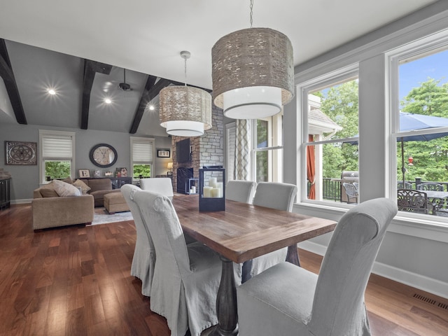 dining space with lofted ceiling with beams, dark wood-style floors, baseboards, and a large fireplace