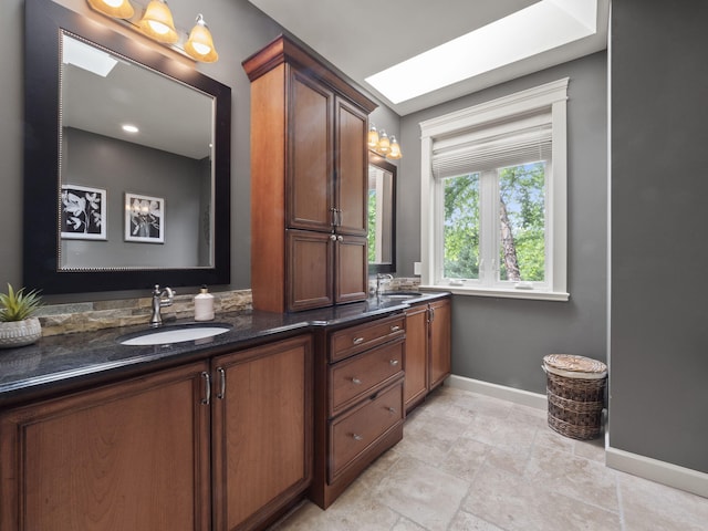 full bath featuring double vanity, a skylight, baseboards, and a sink