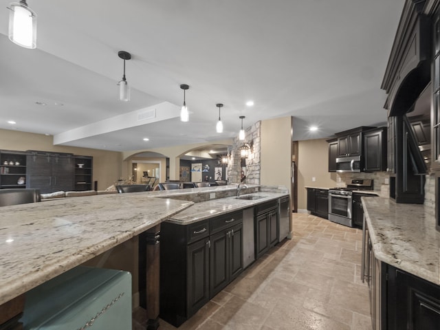 kitchen with visible vents, dark cabinetry, stone tile flooring, arched walkways, and appliances with stainless steel finishes