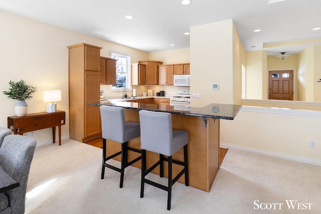 kitchen with sink, dark stone countertops, light colored carpet, white appliances, and a breakfast bar area