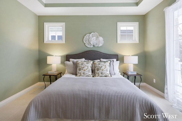 bedroom featuring light carpet, a raised ceiling, and multiple windows