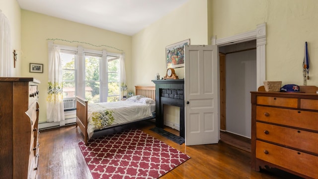 bedroom featuring dark hardwood / wood-style floors, a stone fireplace, and a baseboard radiator