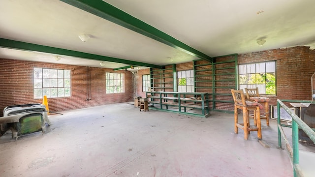 miscellaneous room with concrete flooring, brick wall, and beamed ceiling