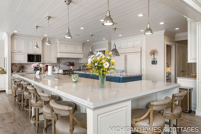 kitchen featuring a kitchen bar, a large island, decorative light fixtures, and built in appliances