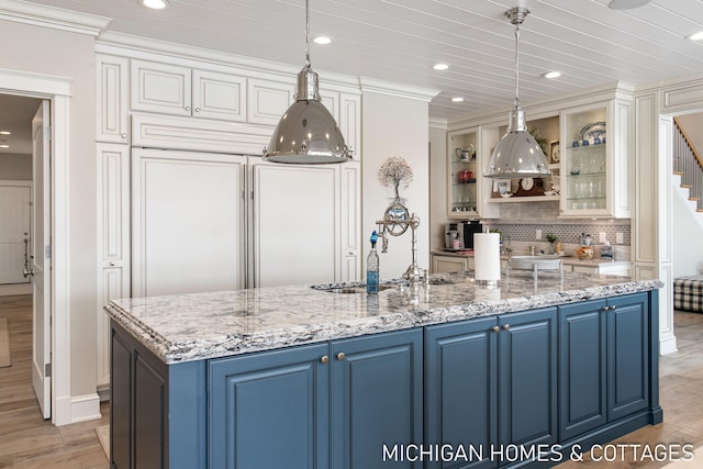 kitchen featuring blue cabinetry, sink, hanging light fixtures, light stone countertops, and light hardwood / wood-style floors