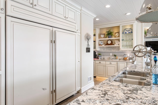 kitchen featuring sink, crown molding, light hardwood / wood-style flooring, light stone countertops, and decorative backsplash