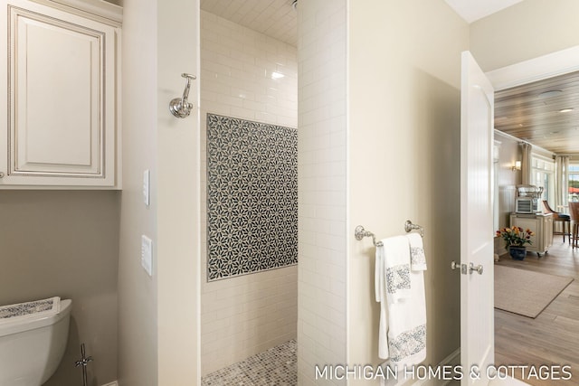 bathroom with wood-type flooring, a tile shower, and toilet