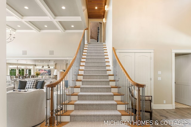 stairway featuring beamed ceiling, wood-type flooring, coffered ceiling, and a high ceiling