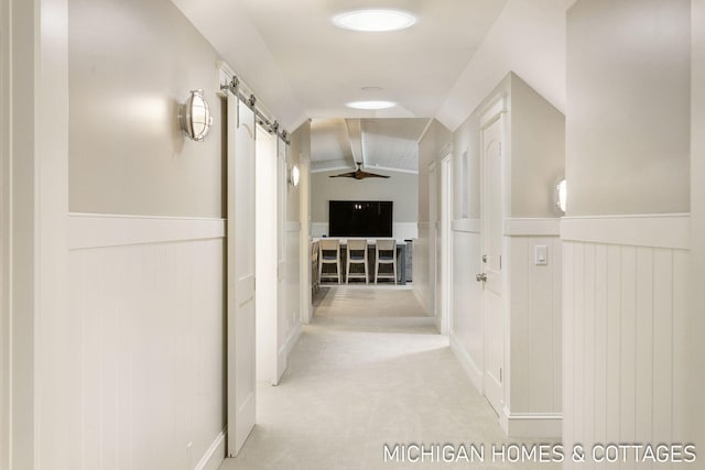 hall featuring light colored carpet, lofted ceiling, and a barn door