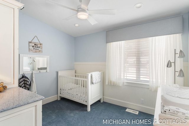 bedroom with a crib, dark carpet, and ceiling fan