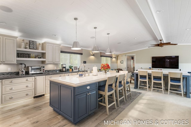 kitchen featuring a kitchen bar, decorative light fixtures, lofted ceiling with beams, light hardwood / wood-style flooring, and a kitchen island with sink