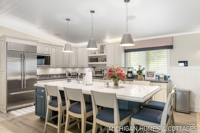 kitchen featuring vaulted ceiling, built in appliances, a kitchen island with sink, and hanging light fixtures