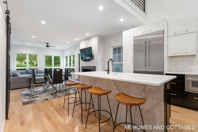 kitchen featuring light hardwood / wood-style floors, appliances with stainless steel finishes, a large fireplace, and a kitchen island with sink