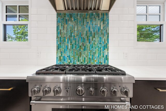 kitchen with high end stove, a healthy amount of sunlight, decorative backsplash, and wall chimney exhaust hood