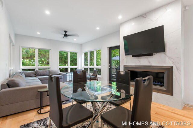 dining room with a healthy amount of sunlight, a premium fireplace, ceiling fan, and light hardwood / wood-style floors