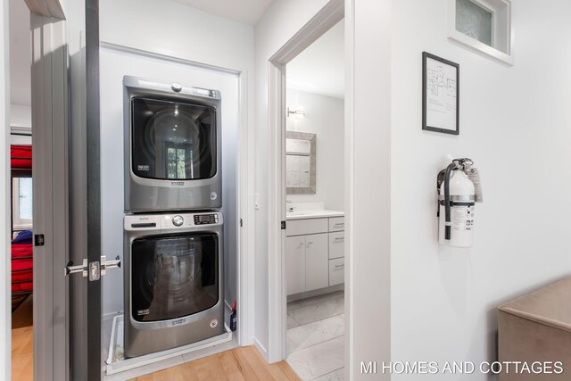 laundry area with stacked washing maching and dryer and light hardwood / wood-style flooring