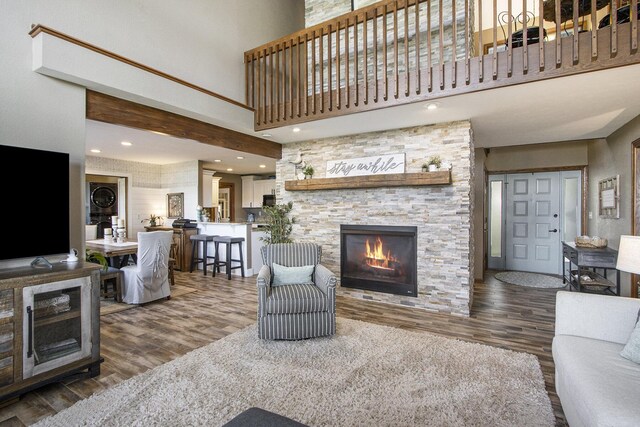 living room with wood-type flooring, a fireplace, stacked washer and dryer, and a towering ceiling