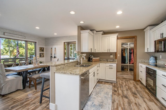 kitchen featuring light wood-type flooring, plenty of natural light, black appliances, sink, and kitchen peninsula