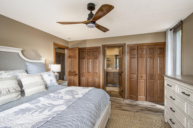 bedroom with ceiling fan, light hardwood / wood-style flooring, ensuite bath, and two closets