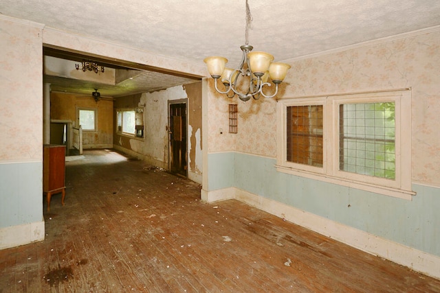 empty room with wood-type flooring, a textured ceiling, ornamental molding, and an inviting chandelier