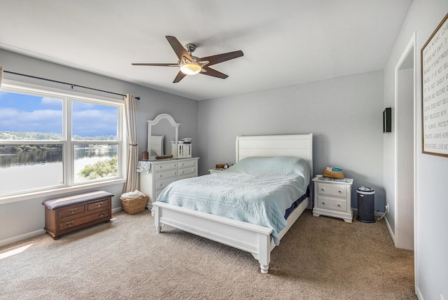 bedroom with light colored carpet, ceiling fan, and a water view