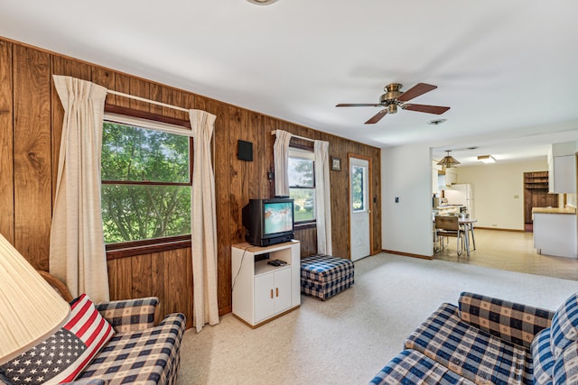 living room featuring ceiling fan, wood walls, and a healthy amount of sunlight