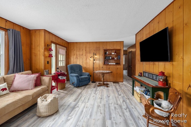 living room with light wood-type flooring, a textured ceiling, and wood walls