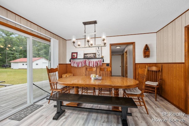 dining space with wooden walls, a chandelier, light hardwood / wood-style floors, and a textured ceiling