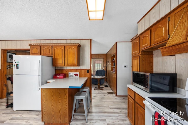 kitchen featuring light hardwood / wood-style flooring, wooden walls, a kitchen breakfast bar, white refrigerator, and range with electric stovetop