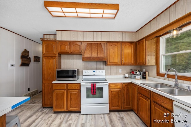 kitchen with wooden walls, sink, light wood-type flooring, custom exhaust hood, and white appliances