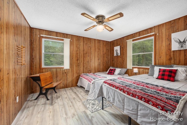 bedroom featuring ceiling fan, wood walls, a textured ceiling, and light wood-type flooring