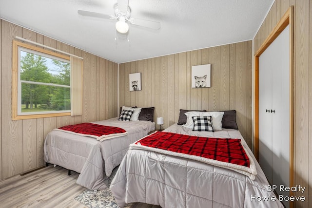 bedroom featuring ceiling fan, wooden walls, hardwood / wood-style floors, and a closet